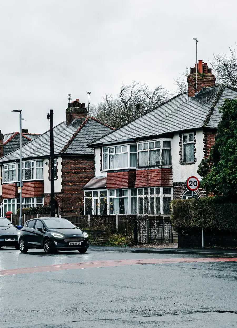 A row of semi-detached houses with tiled roofs and chimneys on a wet street