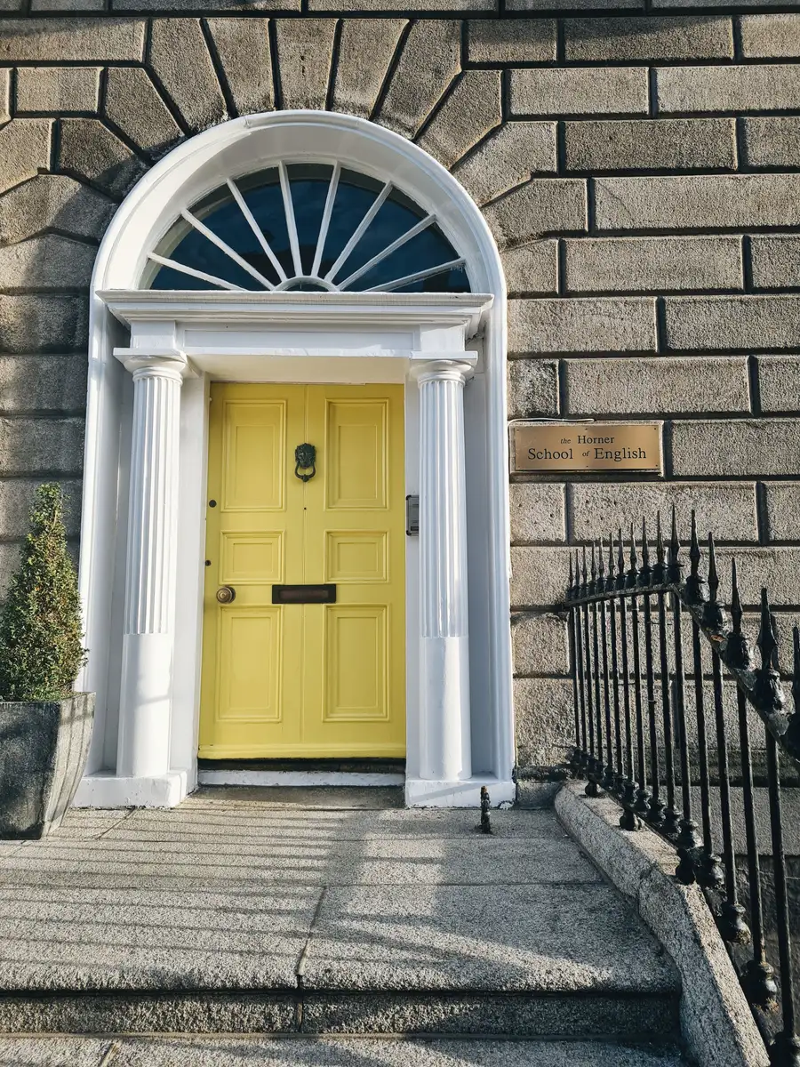A yellow Georgian front door with a fanlight, stone steps and black iron railings