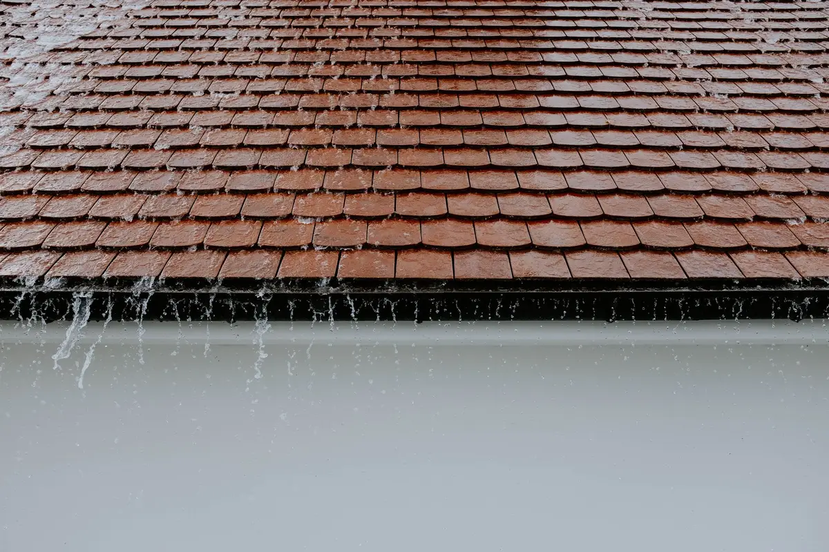 Rain running off the bottom edge of a tiled roof into a white gutter