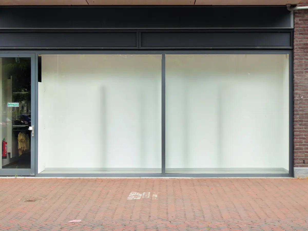 An empty modern retail storefront with large windows and a block-paved forecourt